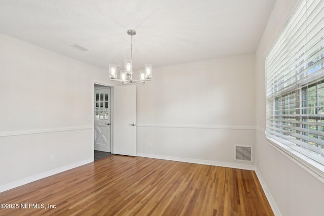 empty room with a notable chandelier, plenty of natural light, wood finished floors, and visible vents