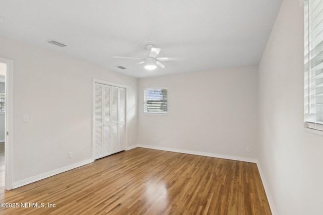 unfurnished bedroom featuring wood finished floors, visible vents, a closet, and baseboards