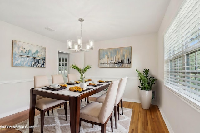 dining room featuring a notable chandelier, baseboards, visible vents, and wood finished floors