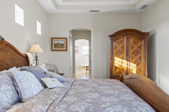 bedroom featuring arched walkways, a raised ceiling, and visible vents