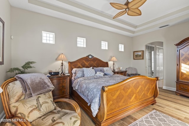 bedroom with light wood finished floors, baseboards, visible vents, arched walkways, and a tray ceiling