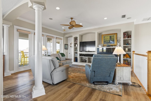 living area featuring built in features, arched walkways, a ceiling fan, wood finished floors, and ornate columns