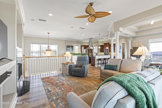 living room featuring crown molding, recessed lighting, light wood-style floors, a ceiling fan, and ornate columns