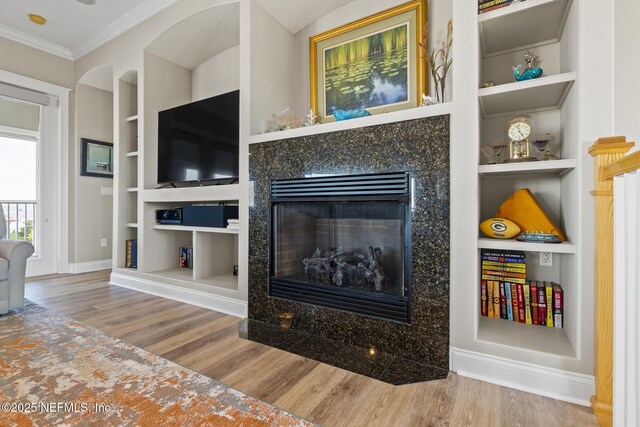 living room with built in shelves, a premium fireplace, wood finished floors, and crown molding