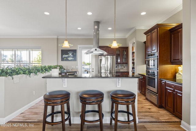kitchen featuring island range hood, stainless steel appliances, a warming drawer, dark countertops, and a kitchen bar