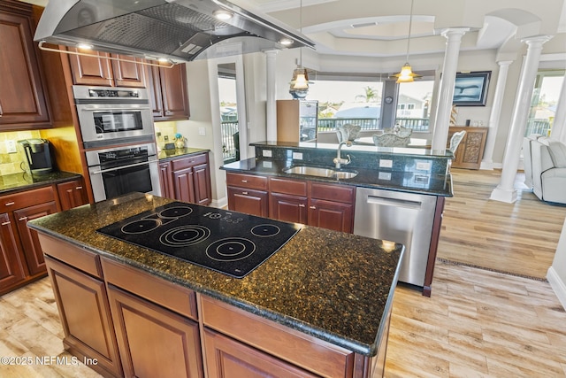 kitchen featuring arched walkways, appliances with stainless steel finishes, a kitchen island with sink, extractor fan, and ornate columns
