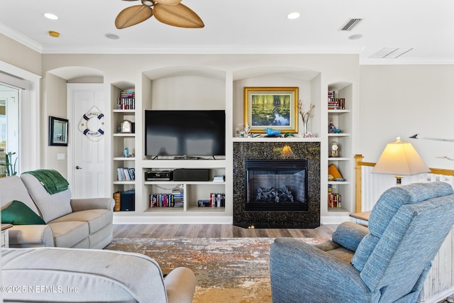 living room with built in features, crown molding, visible vents, a premium fireplace, and wood finished floors
