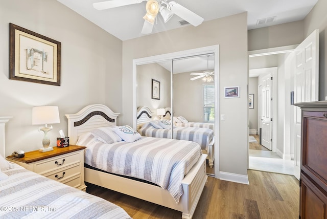 bedroom with wood finished floors, a ceiling fan, visible vents, baseboards, and a closet