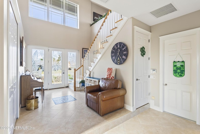 entrance foyer with light tile patterned floors, a towering ceiling, visible vents, baseboards, and stairway