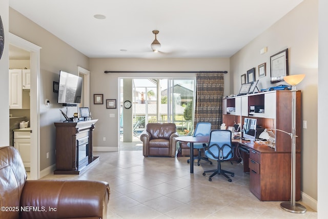 home office with light tile patterned floors, a glass covered fireplace, and baseboards