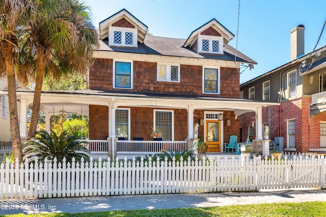 american foursquare style home featuring a fenced front yard, a porch, and roof with shingles