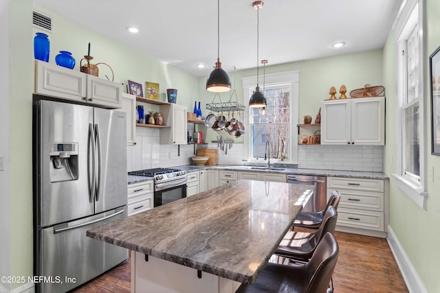 kitchen featuring visible vents, appliances with stainless steel finishes, a kitchen bar, open shelves, and a sink