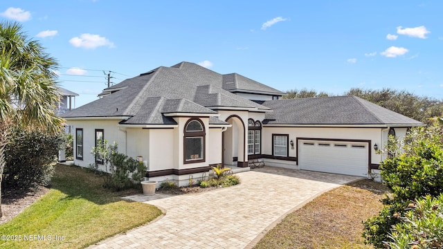 view of front facade featuring a garage, roof with shingles, decorative driveway, a front lawn, and stucco siding