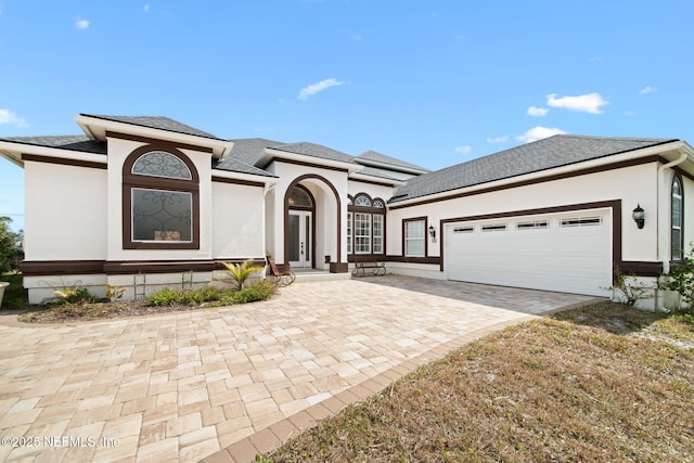 view of front facade featuring an attached garage, driveway, french doors, roof with shingles, and stucco siding