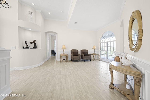 living area featuring arched walkways, wainscoting, and crown molding