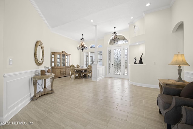 foyer entrance with crown molding, wainscoting, a notable chandelier, and a decorative wall