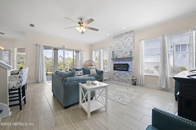 living room featuring visible vents, ornamental molding, ceiling fan, a stone fireplace, and baseboards