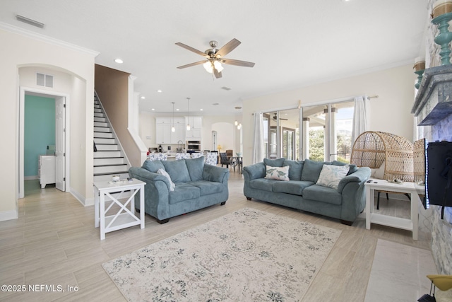 living area featuring light wood finished floors, visible vents, arched walkways, ceiling fan, and stairway