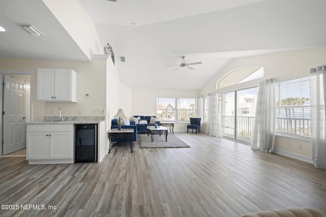 kitchen featuring beverage cooler, wood finished floors, a sink, visible vents, and open floor plan