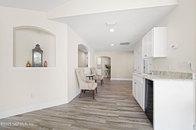 kitchen featuring visible vents, white cabinets, a sink, light wood-type flooring, and baseboards