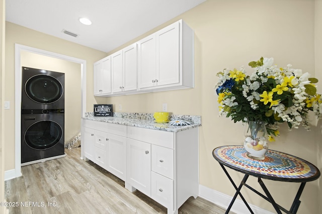 clothes washing area with light wood-style flooring, recessed lighting, stacked washer / dryer, visible vents, and baseboards