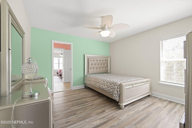 bedroom featuring baseboards, multiple windows, a textured ceiling, and light wood finished floors