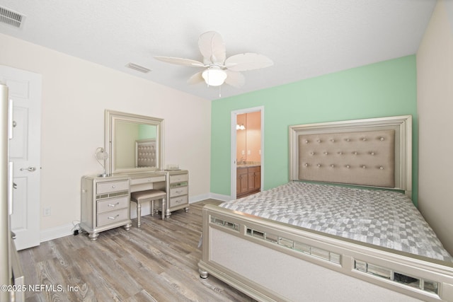 bedroom featuring ensuite bath, baseboards, visible vents, and wood finished floors