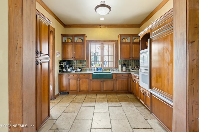 kitchen with oven, decorative backsplash, brown cabinets, and a sink