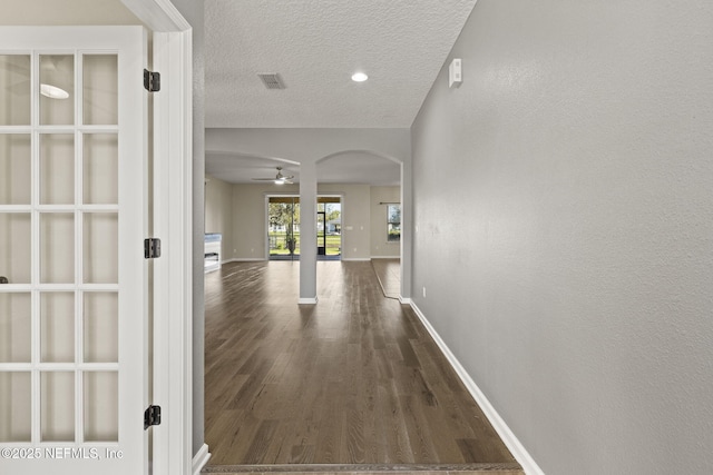 hallway with visible vents, a textured ceiling, wood finished floors, arched walkways, and baseboards