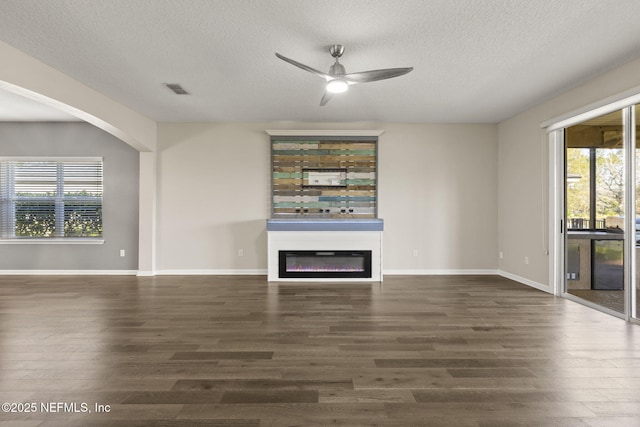 unfurnished living room with a glass covered fireplace, wood finished floors, visible vents, and ceiling fan