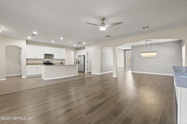 unfurnished living room featuring a ceiling fan, wood finished floors, arched walkways, and visible vents