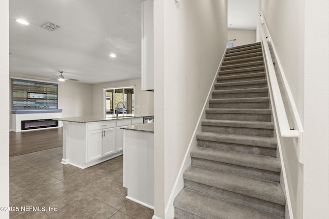 stairs with tile patterned flooring, visible vents, baseboards, a glass covered fireplace, and a ceiling fan