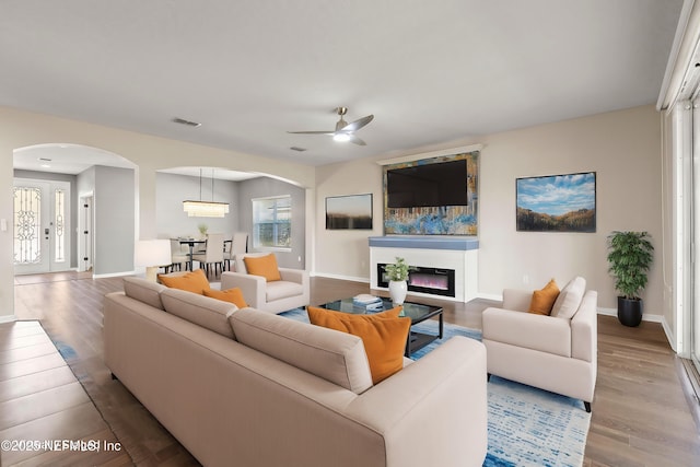 living room with a glass covered fireplace, a wealth of natural light, arched walkways, and wood finished floors