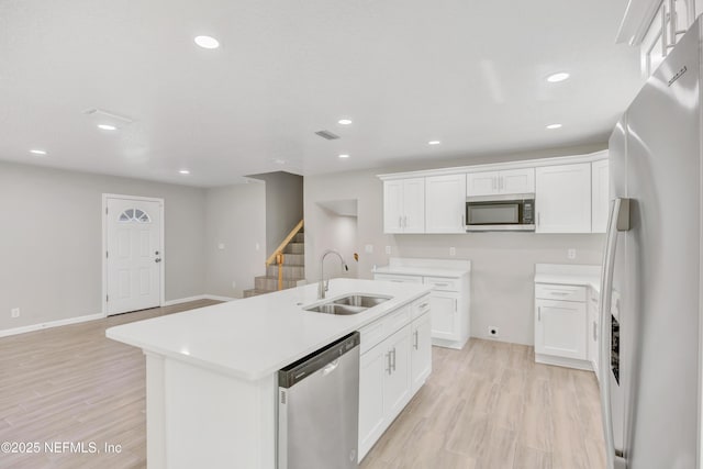 kitchen with light wood finished floors, white cabinetry, stainless steel appliances, and a sink