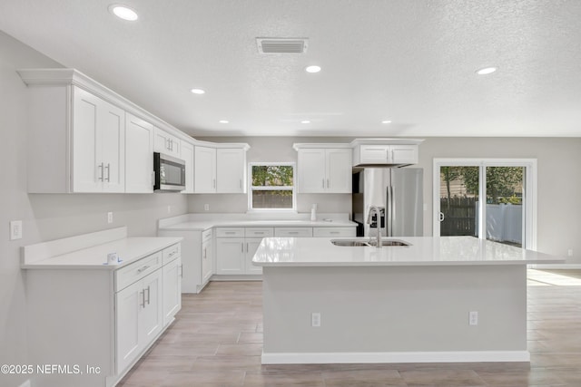 kitchen with a sink, visible vents, white cabinetry, appliances with stainless steel finishes, and a center island with sink