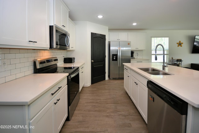 kitchen with appliances with stainless steel finishes, light countertops, a sink, and wood finished floors