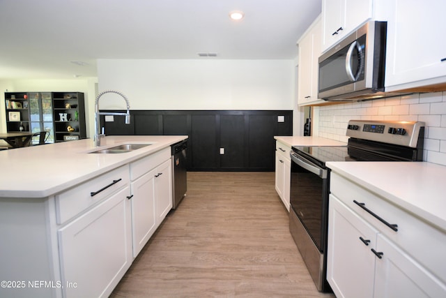 kitchen with white cabinetry, appliances with stainless steel finishes, a sink, and wainscoting