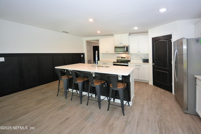 kitchen with decorative backsplash, light wood-style flooring, appliances with stainless steel finishes, a kitchen breakfast bar, and a sink