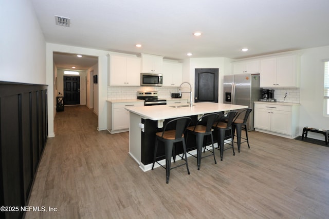 kitchen with a breakfast bar, stainless steel appliances, visible vents, light wood-style flooring, and a sink