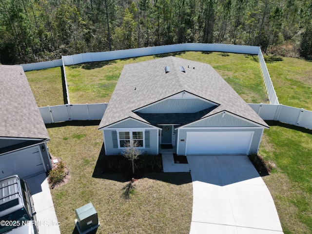 view of front of house with a garage, concrete driveway, a fenced backyard, a front lawn, and a wooded view