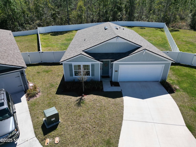 view of front facade featuring an attached garage, a front lawn, a fenced backyard, driveway, and a forest view