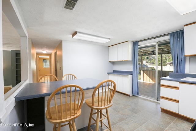 kitchen with dark countertops, white cabinets, visible vents, and a textured ceiling