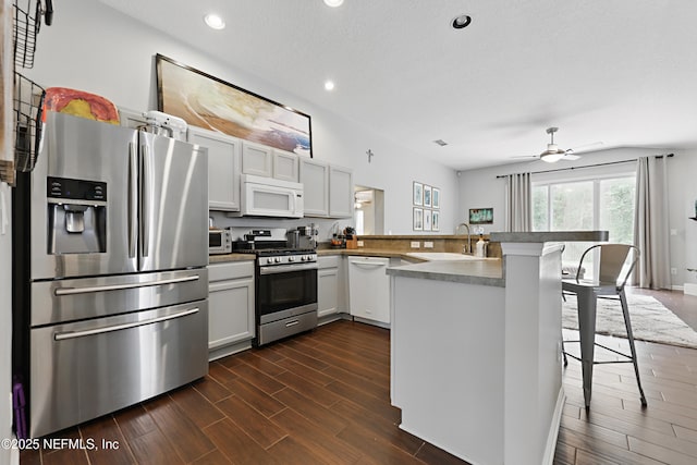 kitchen featuring a breakfast bar area, a peninsula, wood finish floors, a sink, and appliances with stainless steel finishes