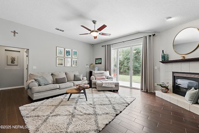 living area with visible vents, dark wood-type flooring, a ceiling fan, a textured ceiling, and a tile fireplace