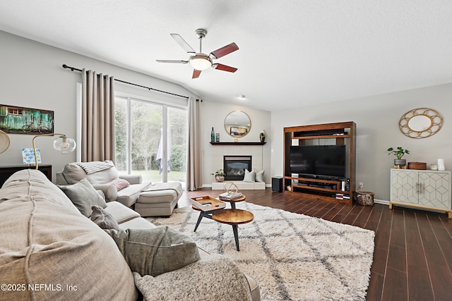 living area with a tiled fireplace, ceiling fan, a textured ceiling, wood finished floors, and baseboards