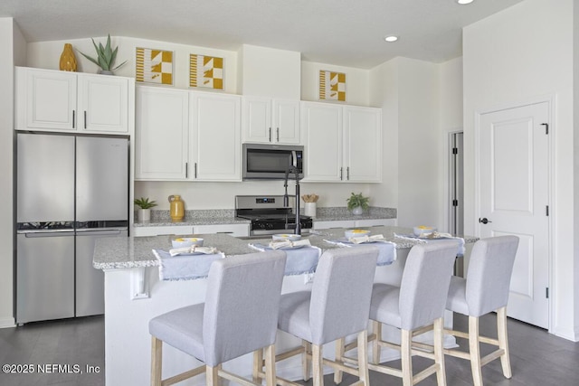 kitchen with stainless steel appliances, a breakfast bar, a kitchen island with sink, and white cabinetry