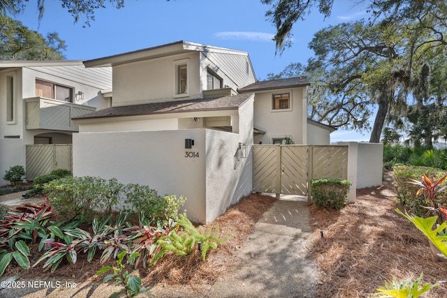 view of property exterior with a shingled roof, a gate, fence, and stucco siding