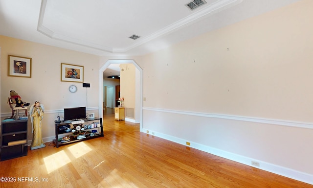 living room with light wood-type flooring, arched walkways, visible vents, and a tray ceiling