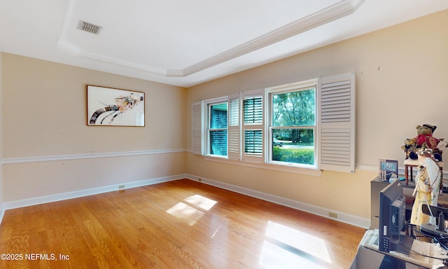 spare room with a tray ceiling, crown molding, visible vents, light wood-style flooring, and baseboards