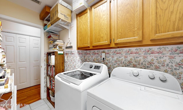 washroom featuring washer and clothes dryer, light tile patterned floors, visible vents, cabinet space, and wallpapered walls